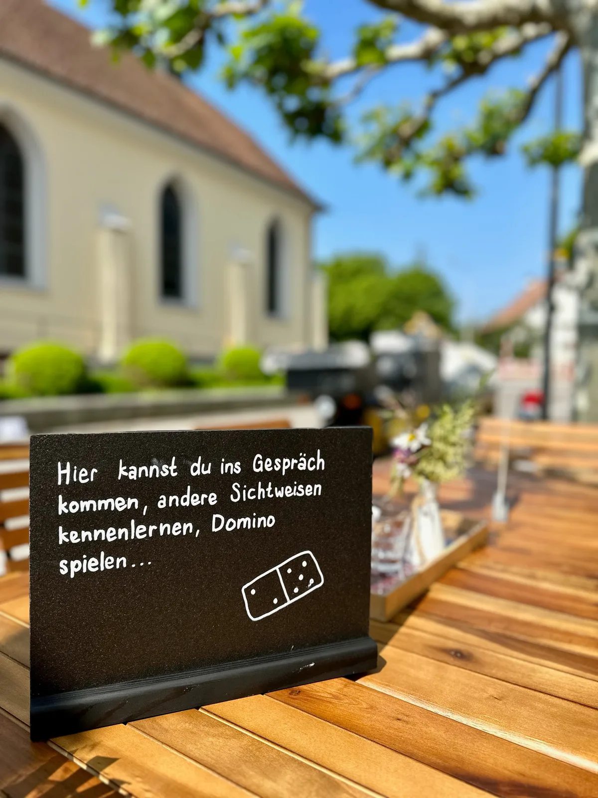 Ein Schild auf dem Begegnungstisch. Darauf steht: «Hier kannst du ins Gespräch kommen und andere Sichtweisen kennenlernen …»